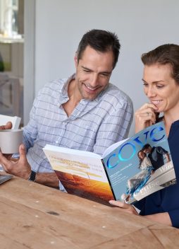 smiling Caucasian couple sitting at outdoor terrace patio having coffee and reading travel magazine