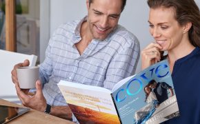 smiling Caucasian couple sitting at outdoor terrace patio having coffee and reading travel magazine